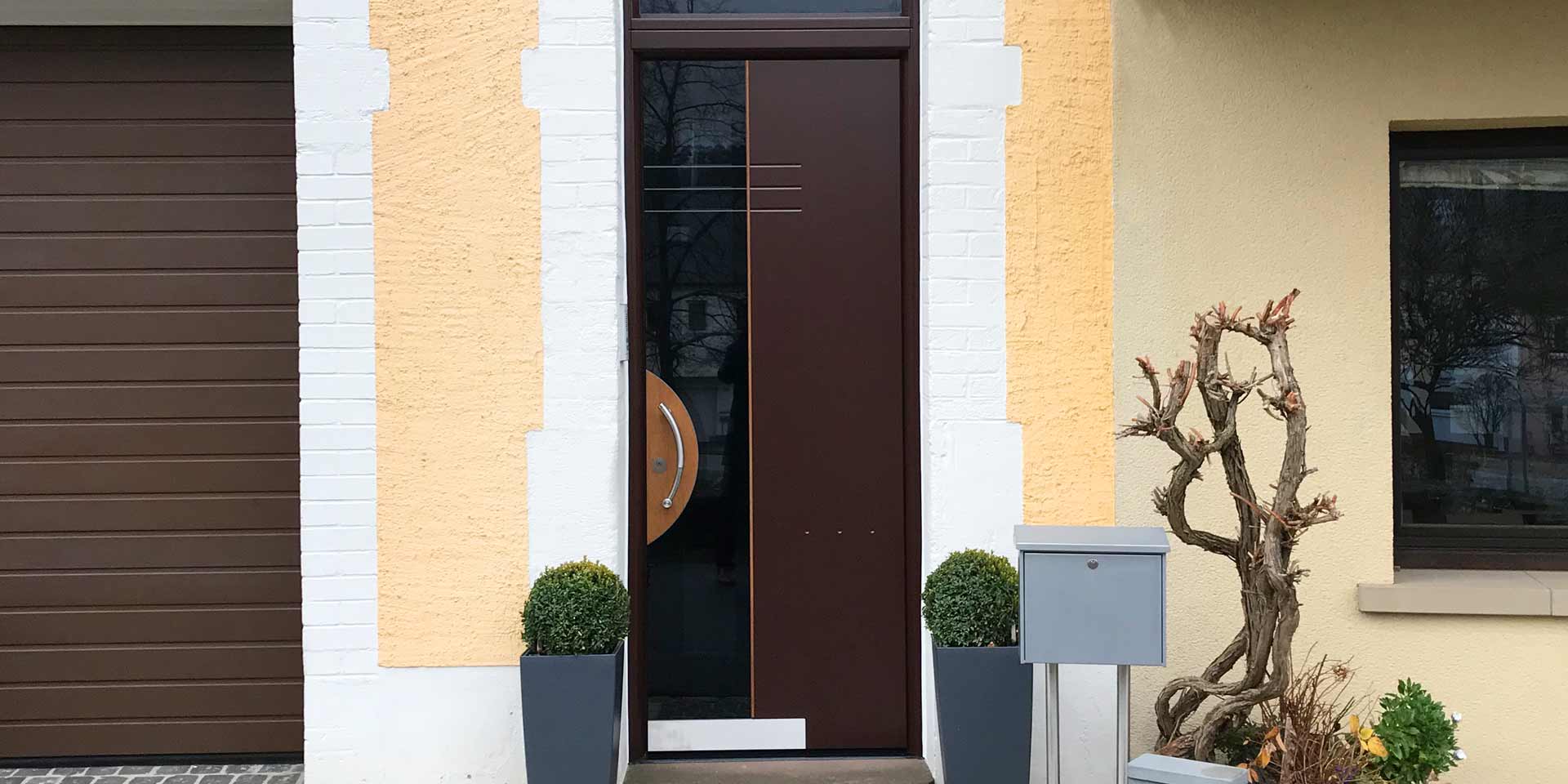 Nahaufnahme auf den Eingangsbereich eines gelben Einfamilienhauses mit Blick auf die neue moderne braune Coplaning Haustür.