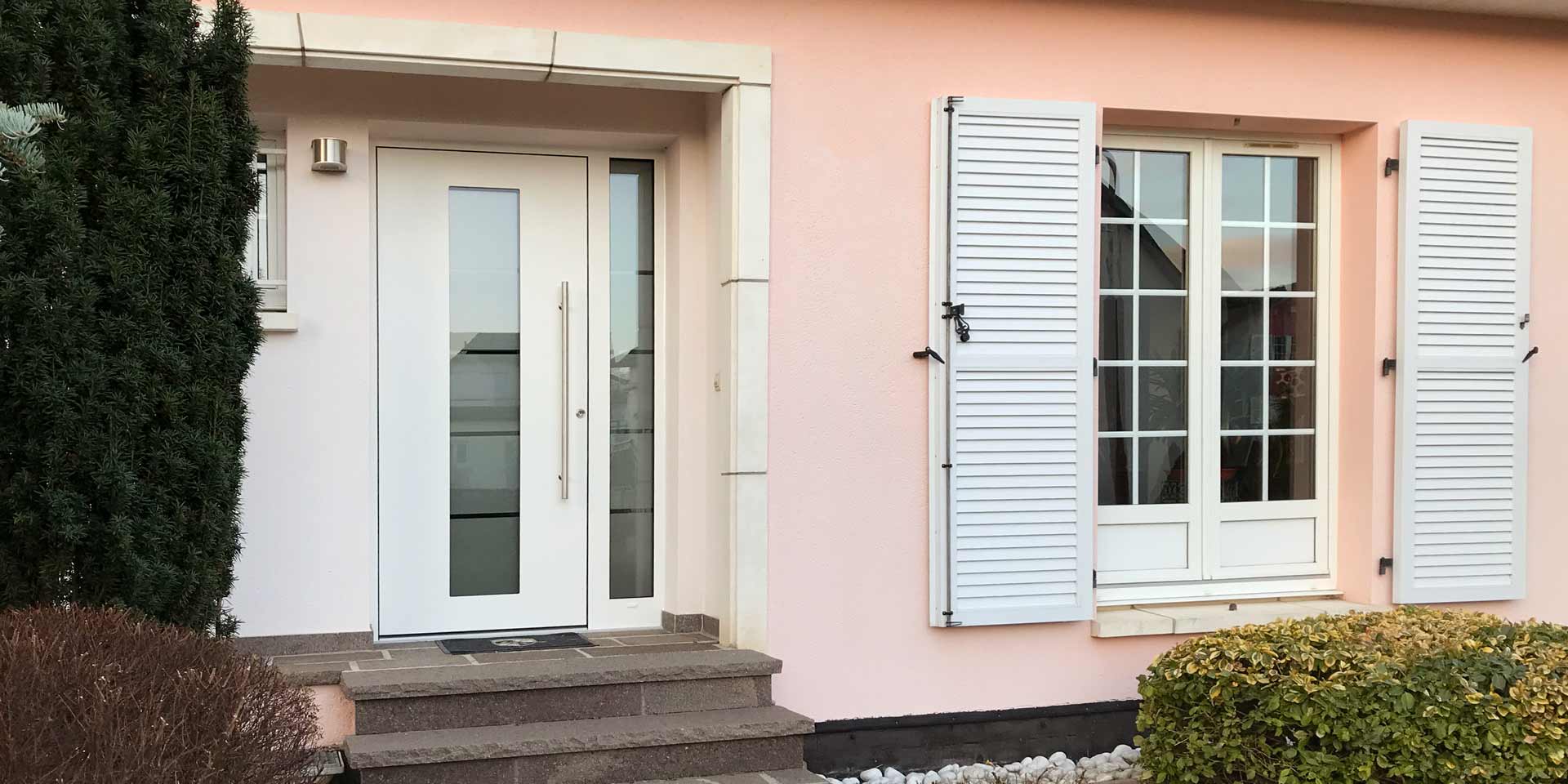 Nahaufnahme vom Eingang des Hauses mit links der neuen weißen Coplaning Haustür aus Keramik und rechts ein weißes Coplaning Holzfenster.