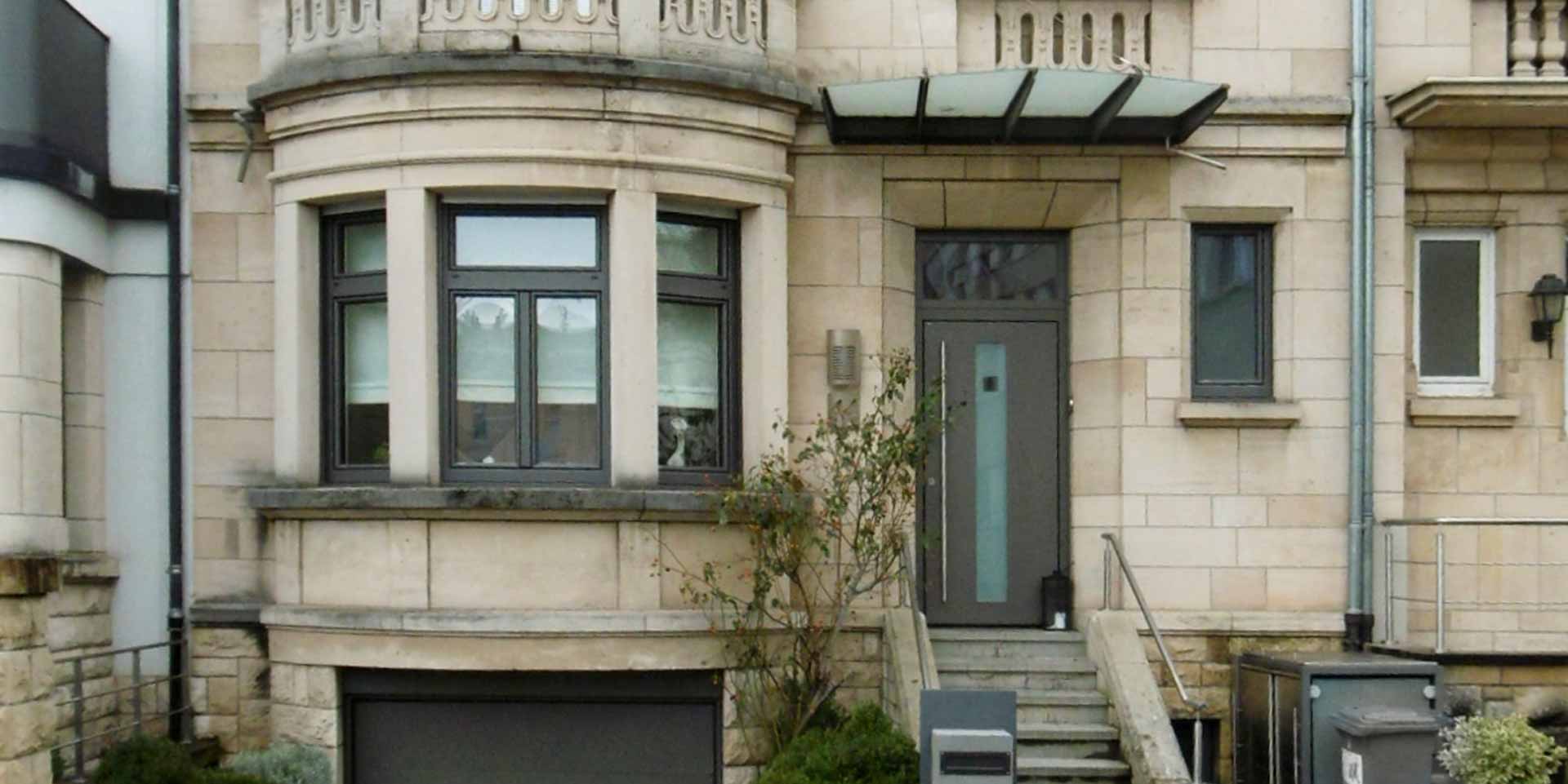 Einfamilienhaus mit Steinfassade mit einer grauen Coplaning Aluminium Haustür und grauen Coplaning Jalousienfenster mit deckensektionaltor.