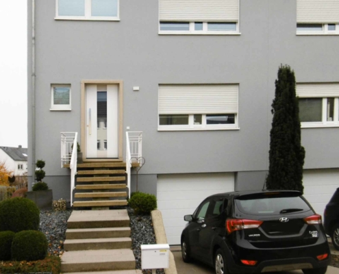 Graues Einfamilienhaus mit neuer moderner weißer Coplaning Haustür.