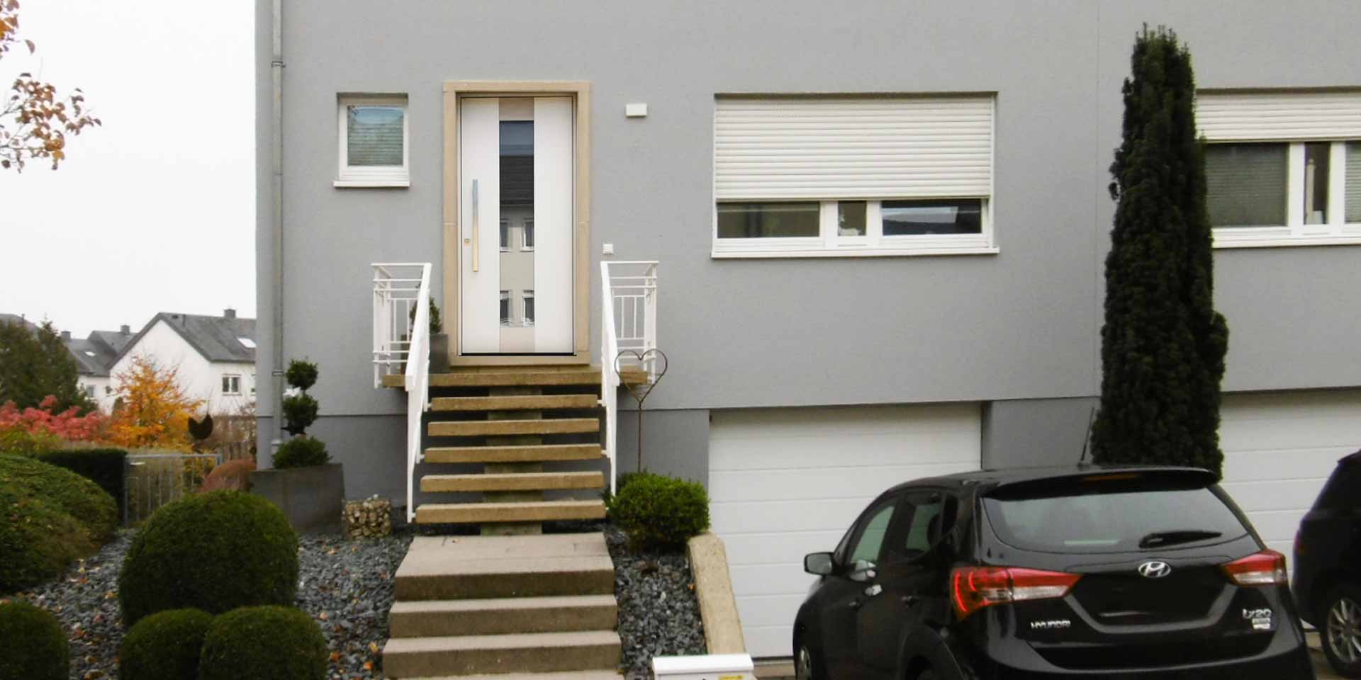 Nahaufnahme des Eingangsbereichs eines grauen Einfamilienhauses mit neuer moderner weißer Coplaning Haustür.